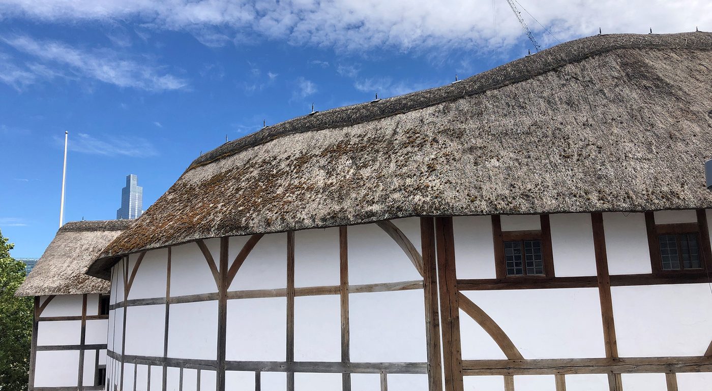 A side view looking at a white wattle and daub theatre, with a blue sky above