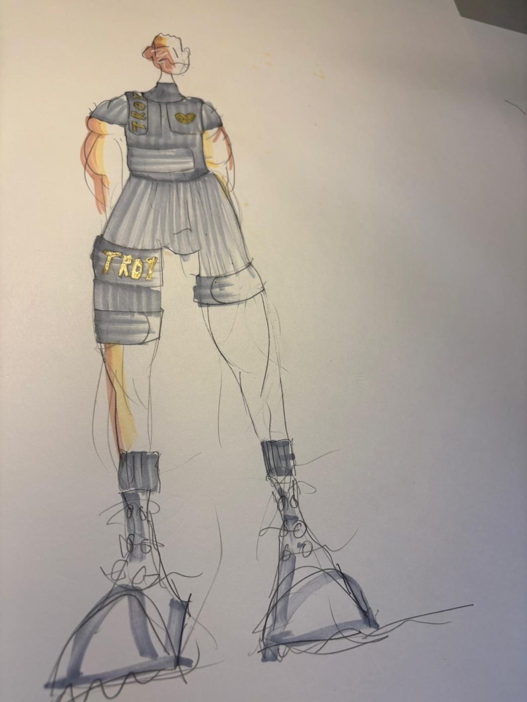 A fashion illustration of a figure wearing grey tactical gear and a legband stating 'Troy' in gold lettering.