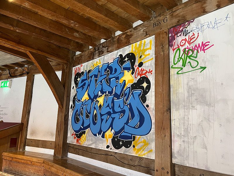 White wall surrounded by wooden beams. The wall is painted with graffiti artwork of the words 'Star crossed'.