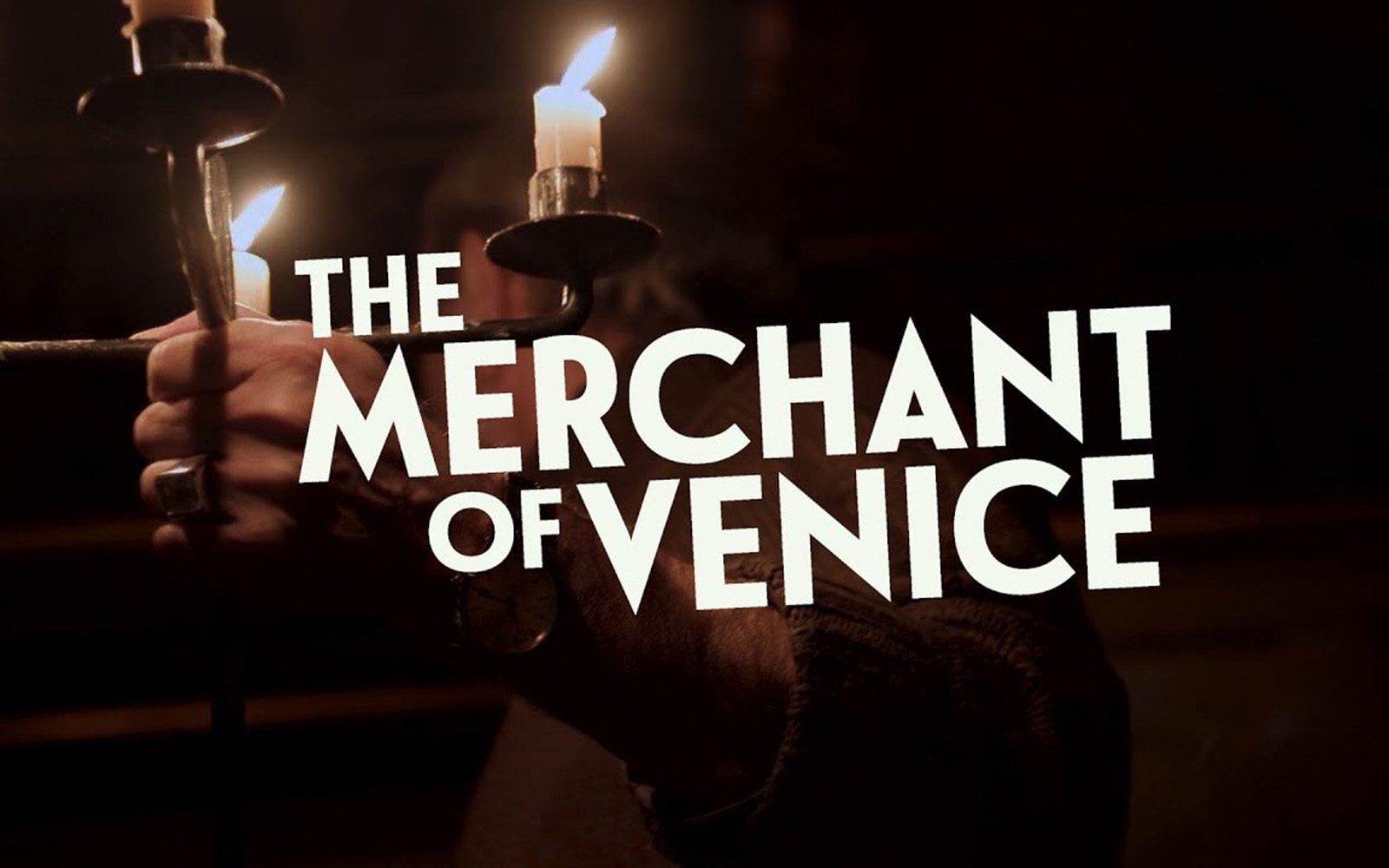 [IMAGE] A hand holds aloft a lit candelabra in a dark, shadowy room. White text reads: The Merchant of Venice